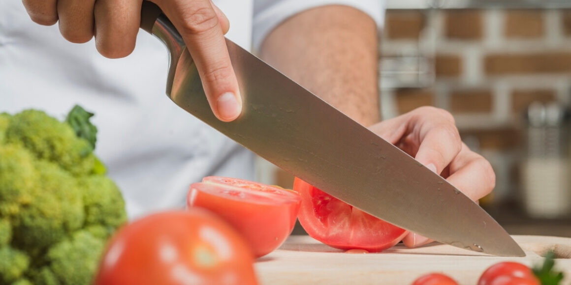 Bannière du quatrième article sur comment choisir ses couteaux, mettant en avant un gros plan sur un couteau qui coupe des tomates