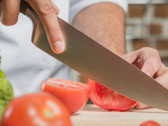 Bannière du quatrième article sur comment choisir ses couteaux, mettant en avant un gros plan sur un couteau qui coupe des tomates