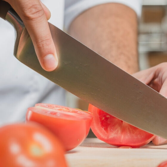 Bannière du quatrième article sur comment choisir ses couteaux, mettant en avant un gros plan sur un couteau qui coupe des tomates